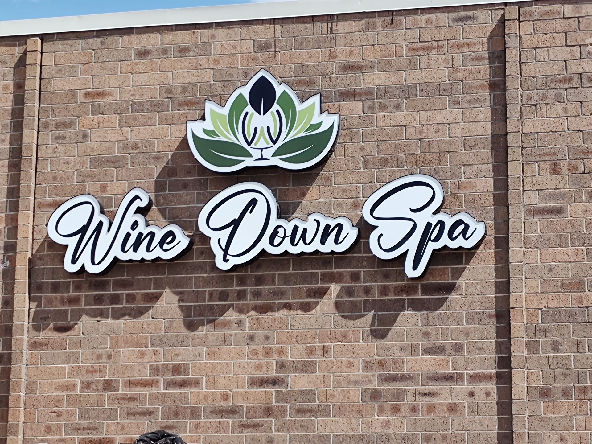 A sign for wine down spa is on a brick wall.