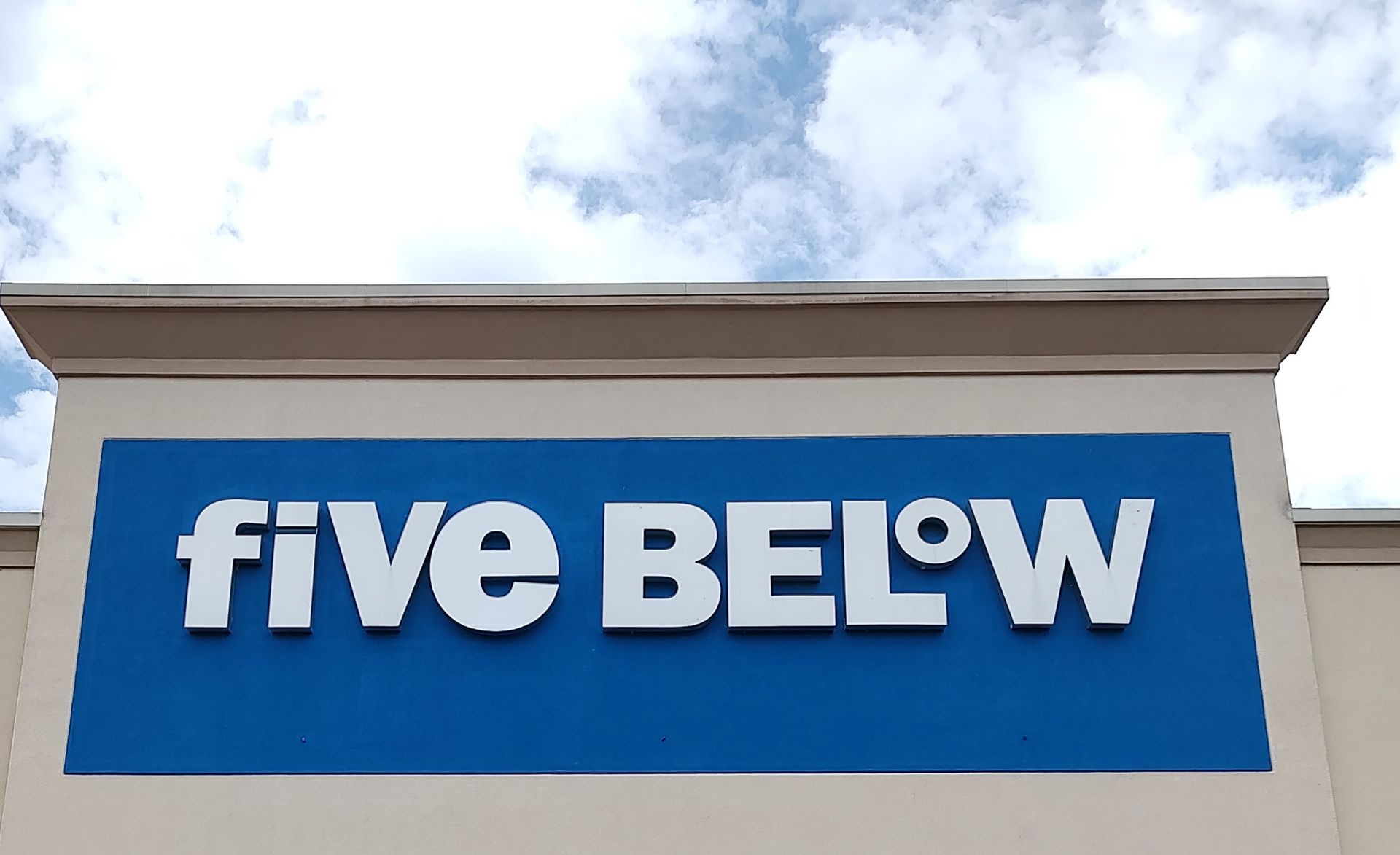 Five Below store sign, blue background with white letters, under cloudy sky.