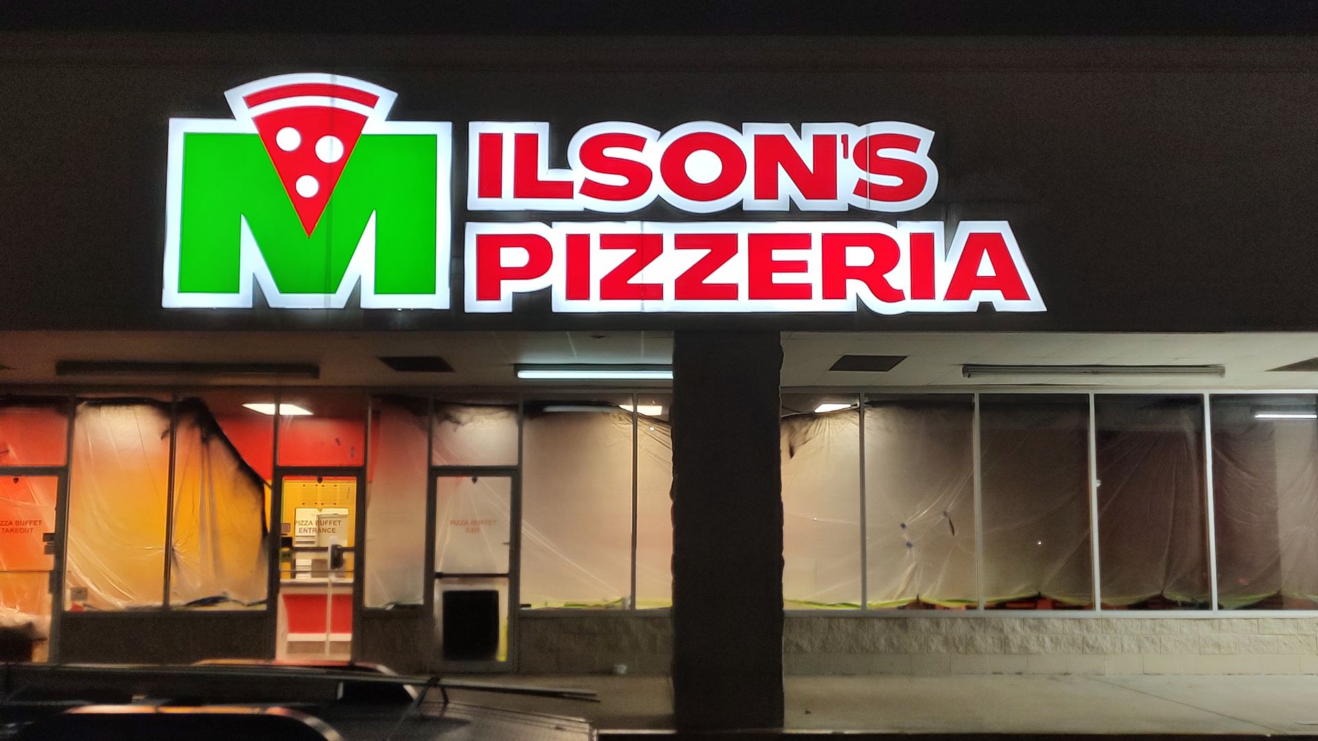 Wilson's Pizzeria sign above a storefront with boarded-up windows at night.