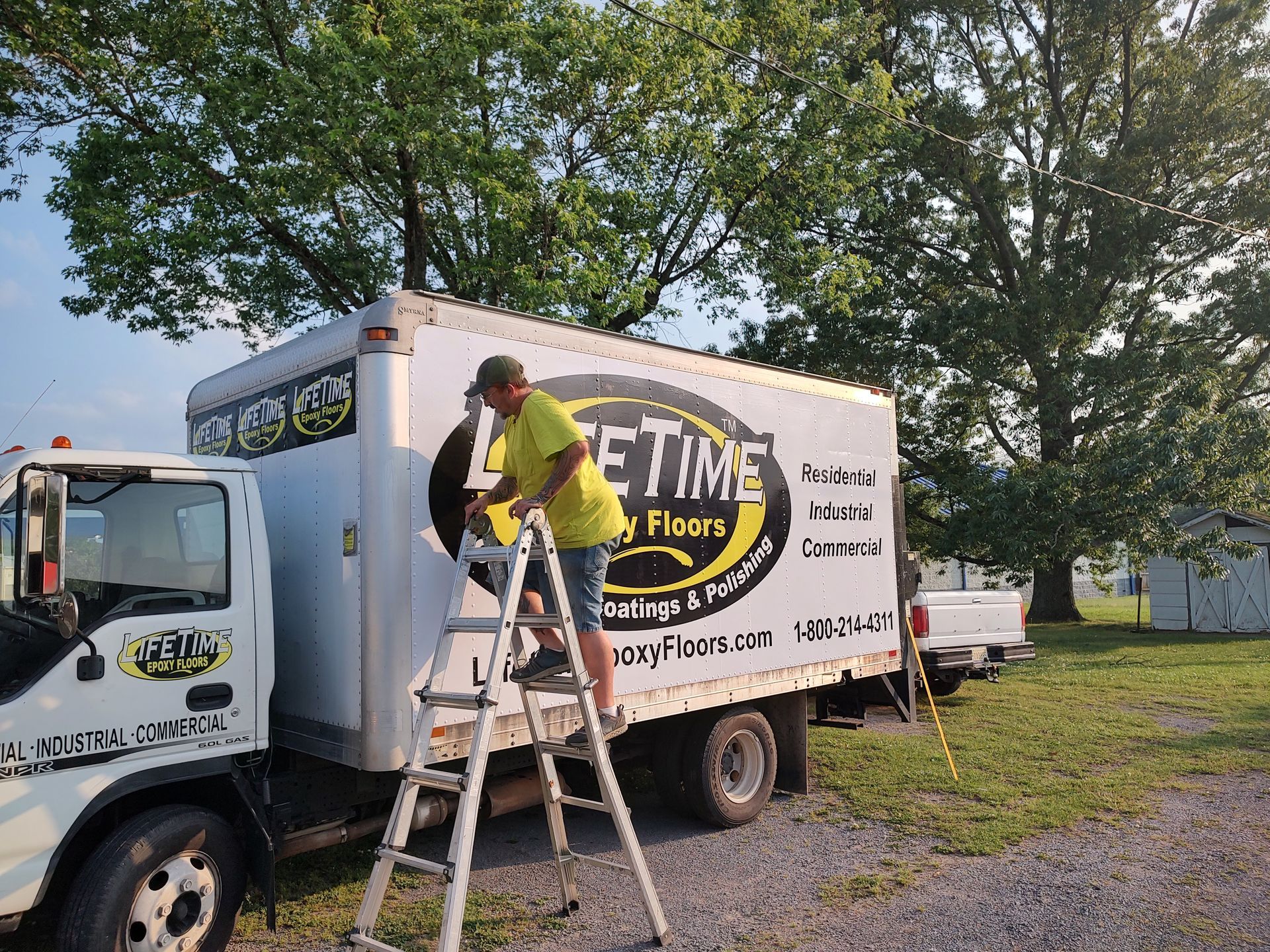 A man is standing on a ladder next to a truck that says etime on it.