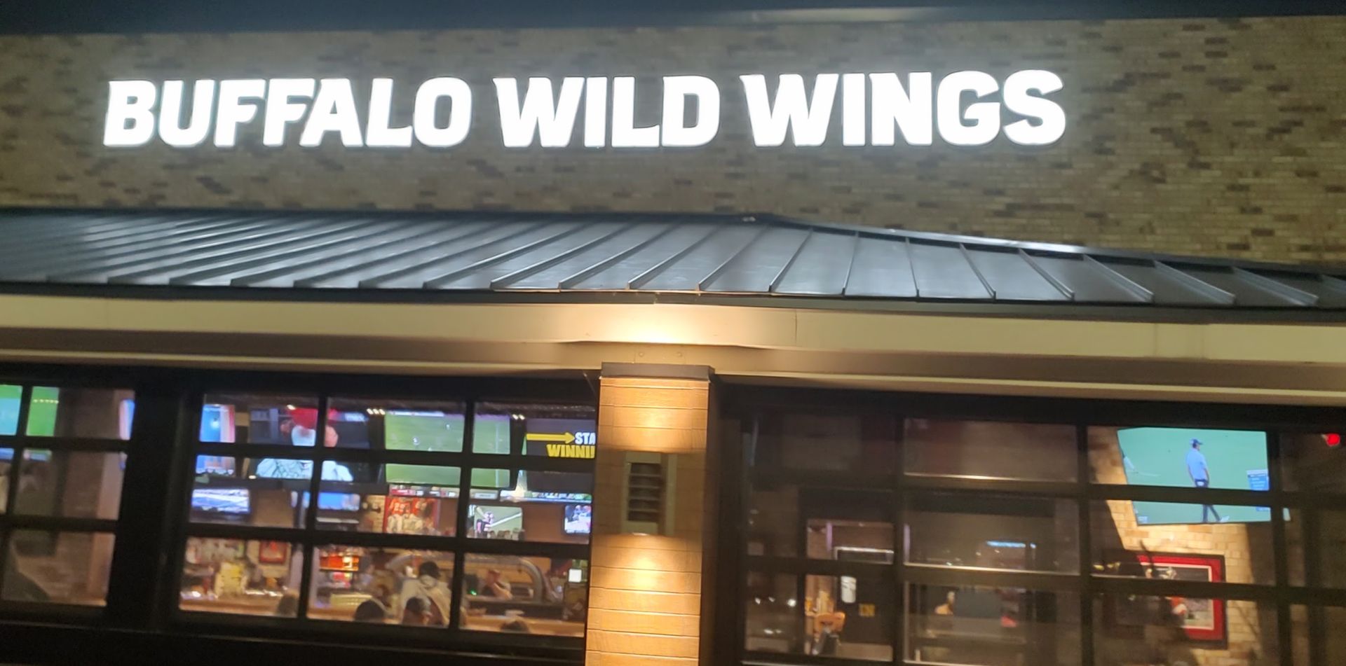Sign of Buffalo Wild Wings above a restaurant's exterior with visible TVs through the windows.
