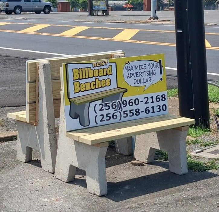 Bench-shaped roadside sign advertising billboard benches with phone numbers beside a street