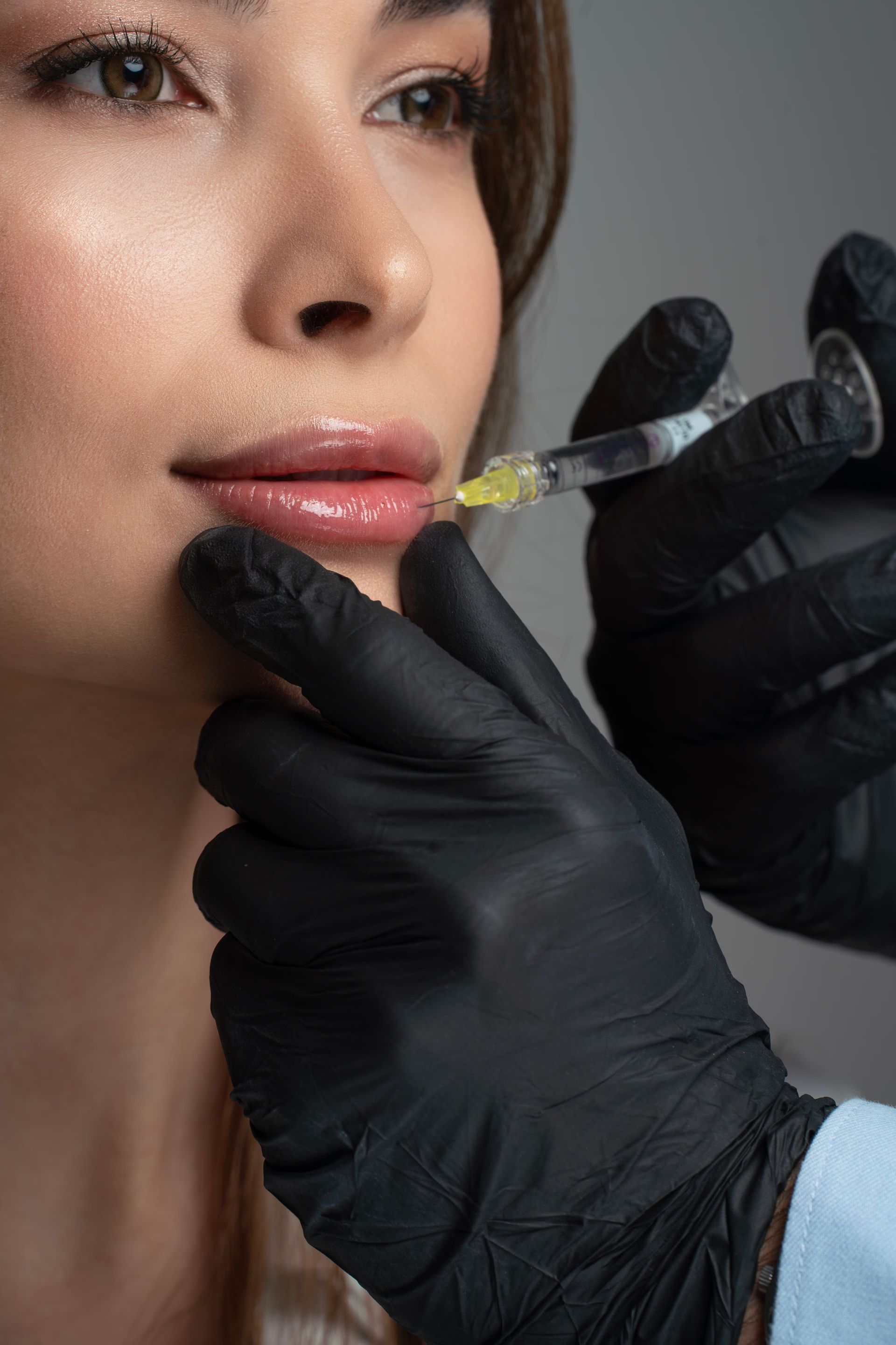 Aesthetic lip injection in progress, with gloved hands applying a syringe to a woman’s lips.
