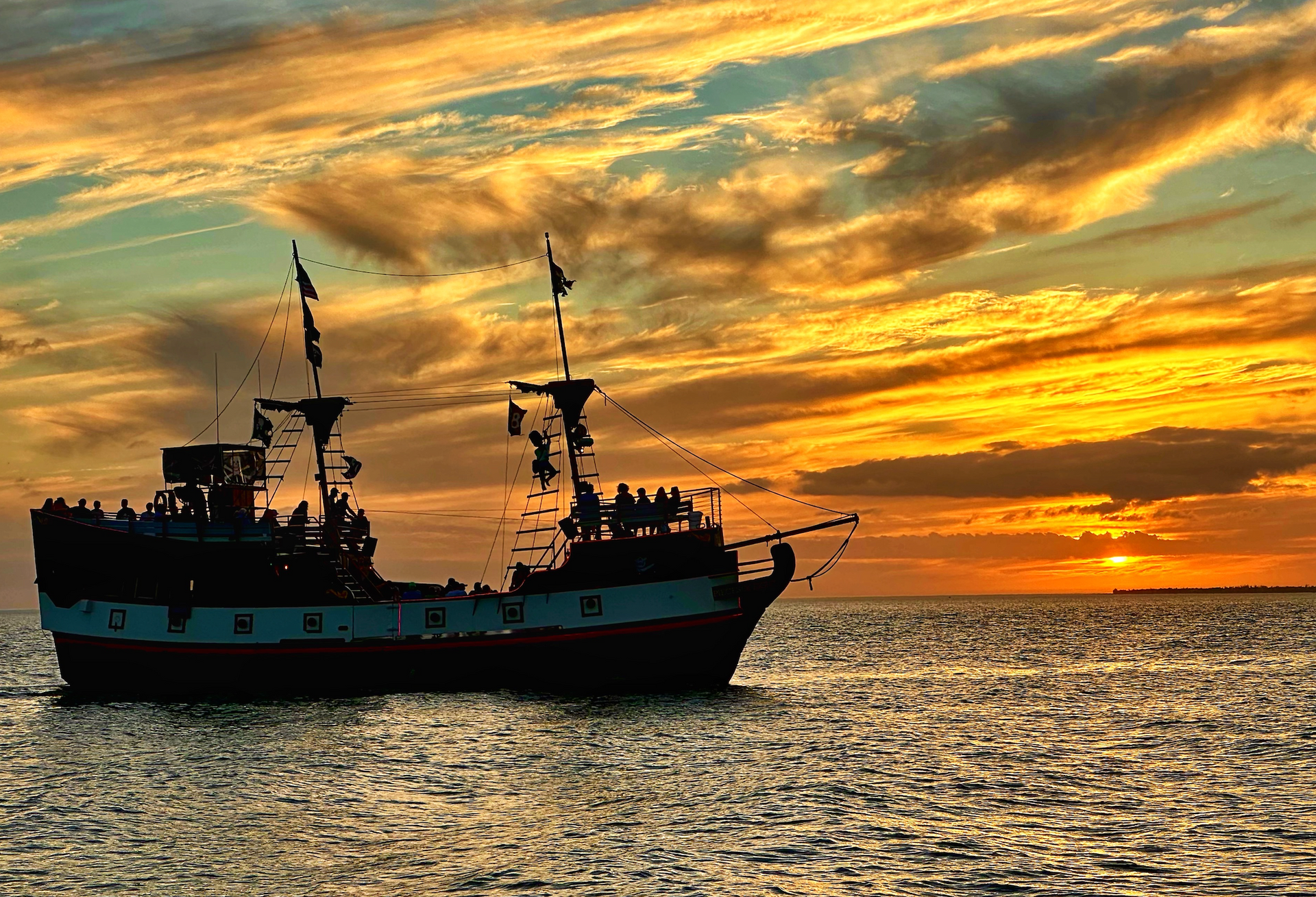 A pirate ship is sailing in the ocean at sunset.