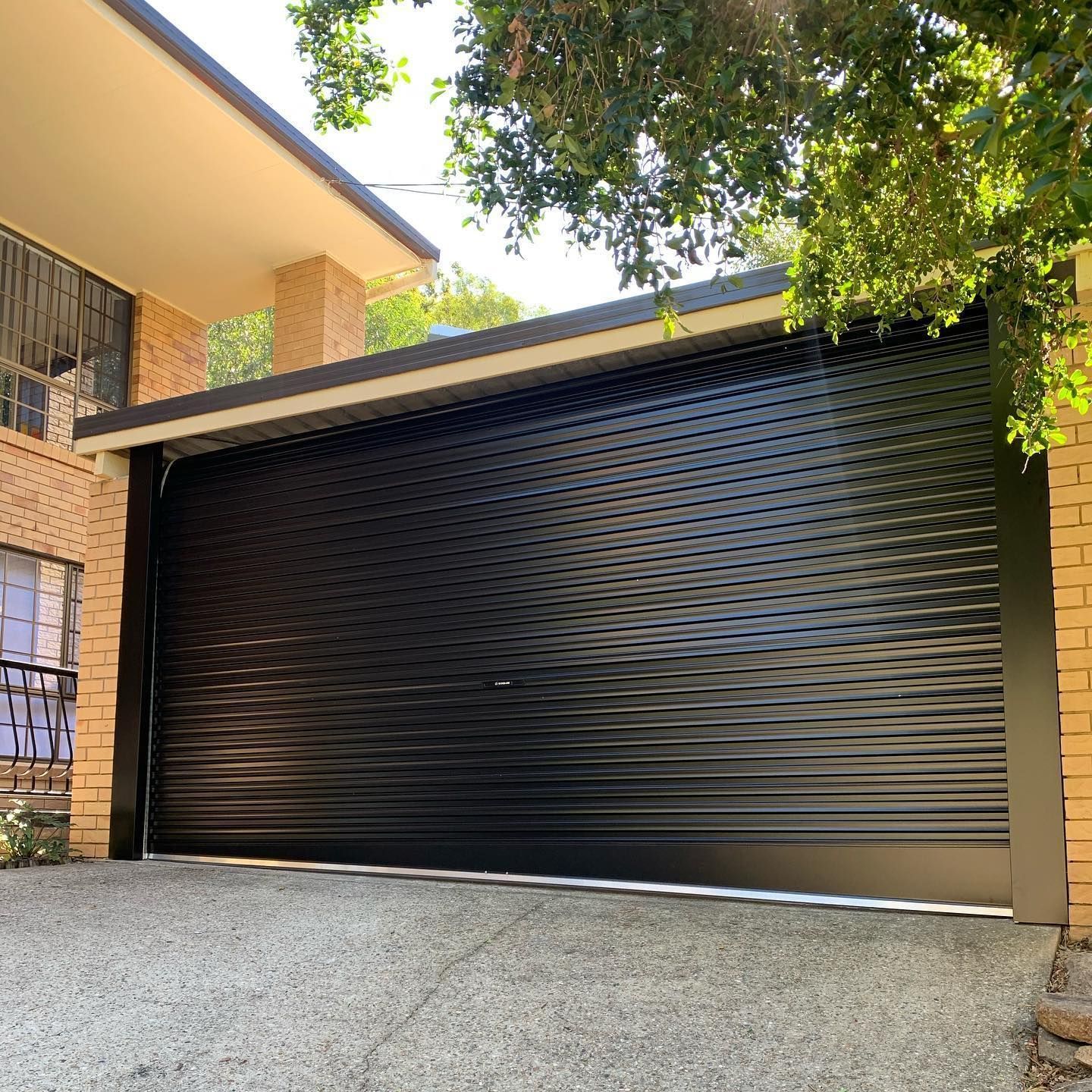 A black garage door is sitting in front of a brick house.