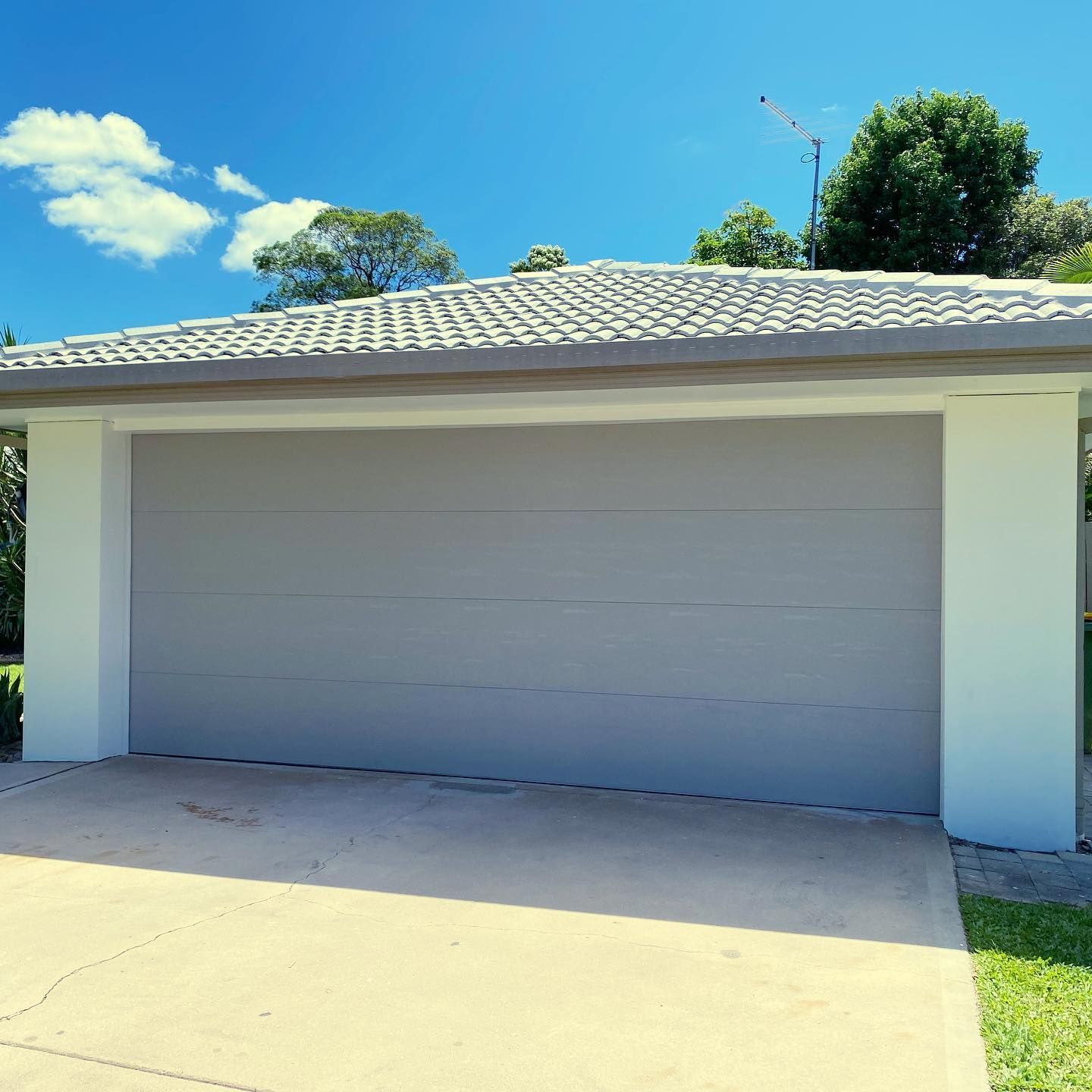 A gray garage door is sitting in front of a house on a sunny day.