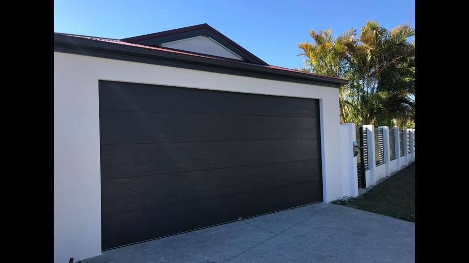 A white house with a black garage door and a fence.