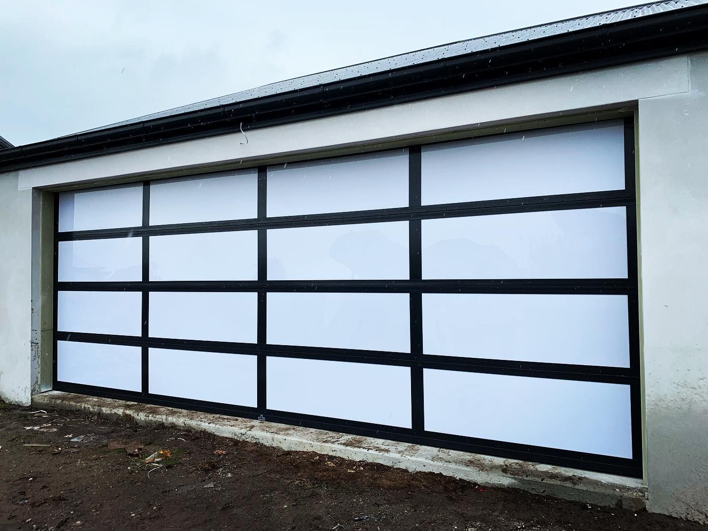 A large white garage door with black trim is sitting on the side of a building.