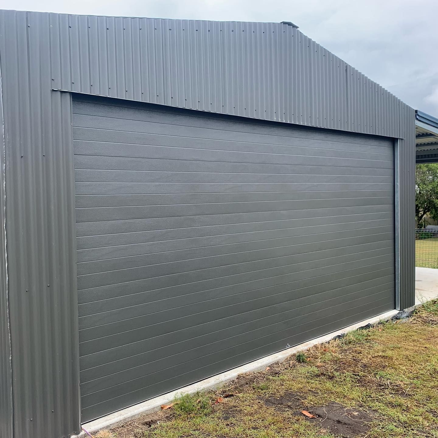 A large gray garage door is sitting in the middle of a grassy field.