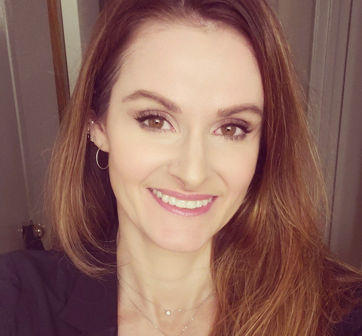 A woman wearing a black jacket and earrings is smiling for the camera.
