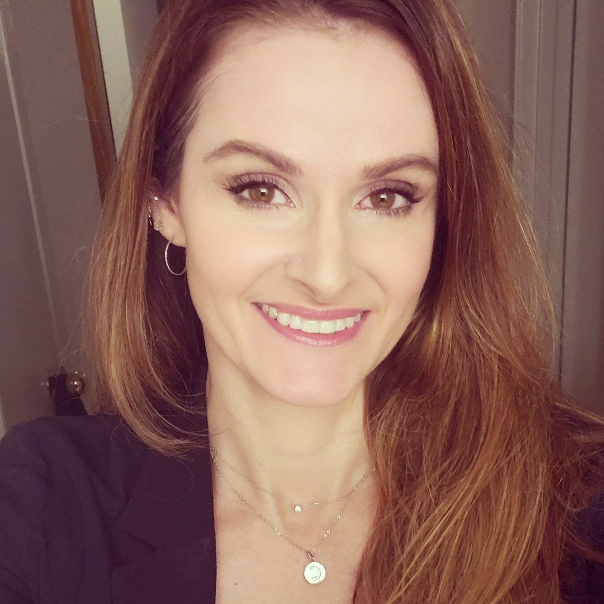 A woman wearing a necklace and earrings is smiling for the camera.