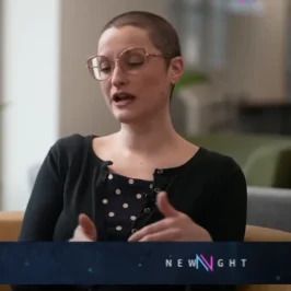 Person speaking in a dim studio, wearing glasses and a black cardigan, with a NEWSNIGHT banner below.