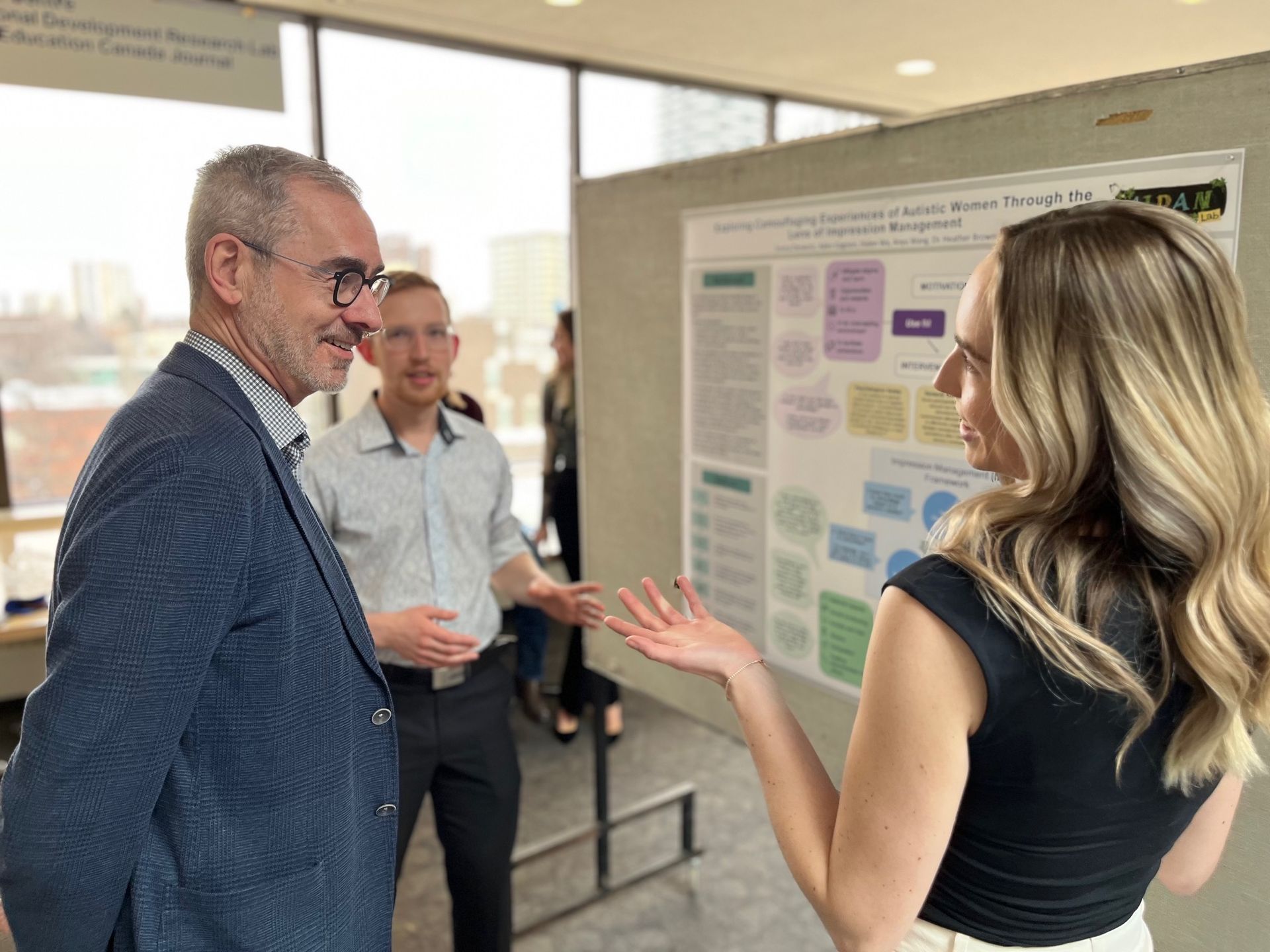 Three people discussing a poster presentation in a bright hallway