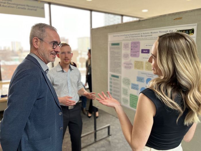 Three people discussing a poster presentation in a bright hallway