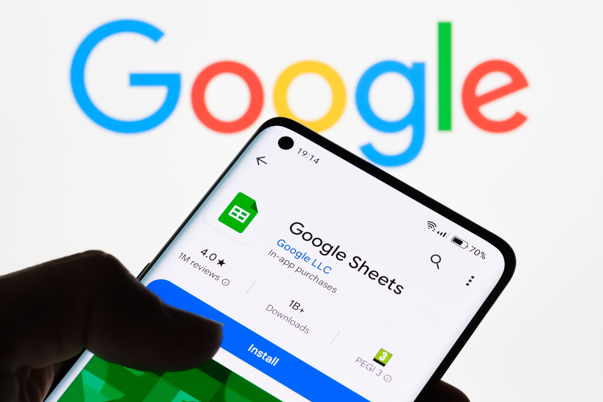 Hand holding phone showing Google Sheets app in front of Google logo