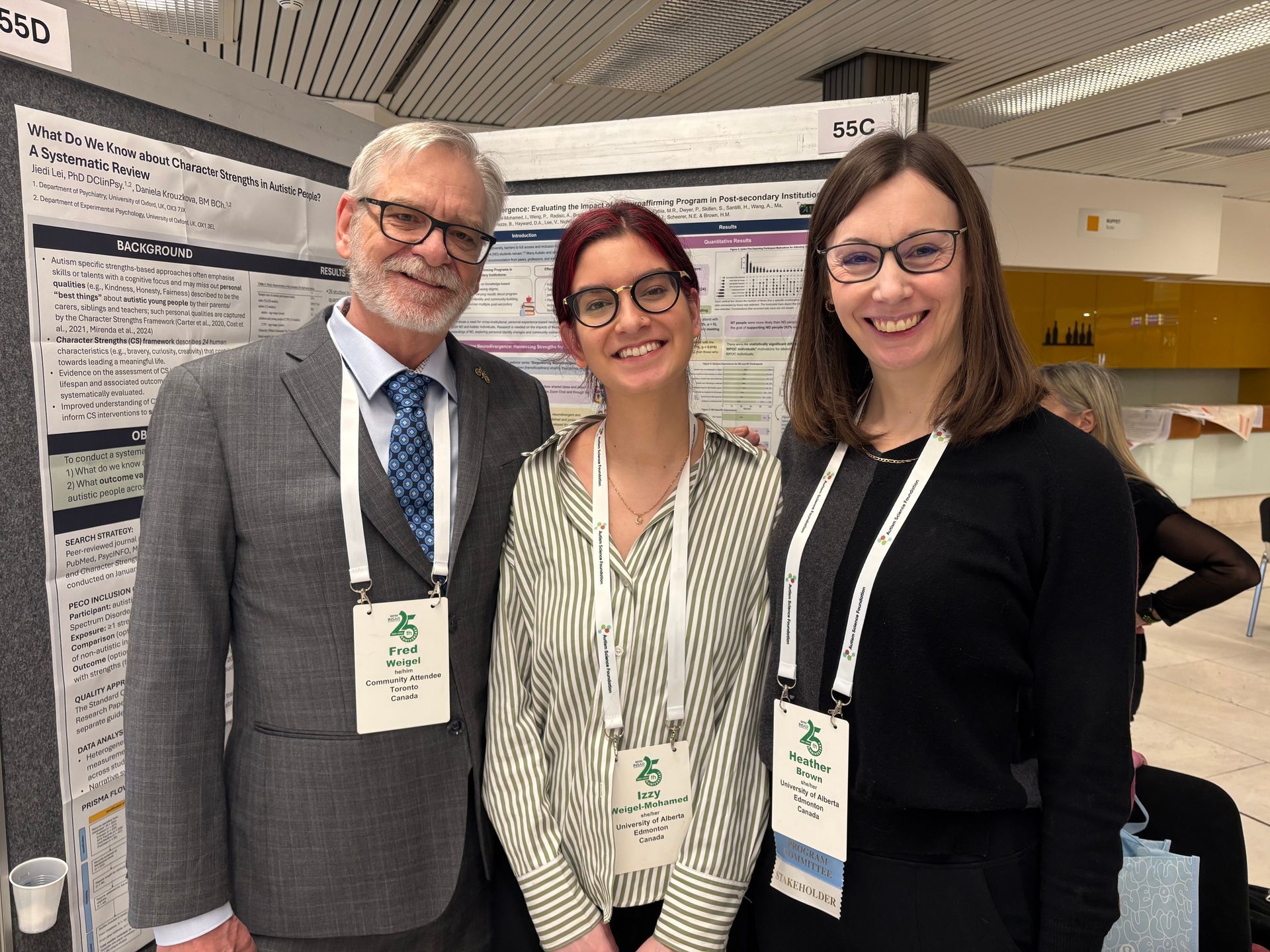 Three people smiling at a conference poster session, standing in front of a presentation board.