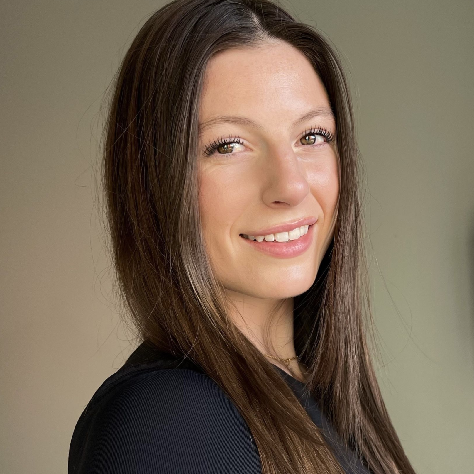 Smiling woman with long brown hair, wearing a black top against a neutral background