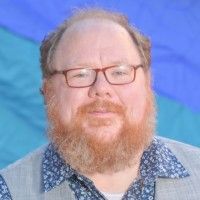 Portrait of a bearded man with glasses against a blue and teal background