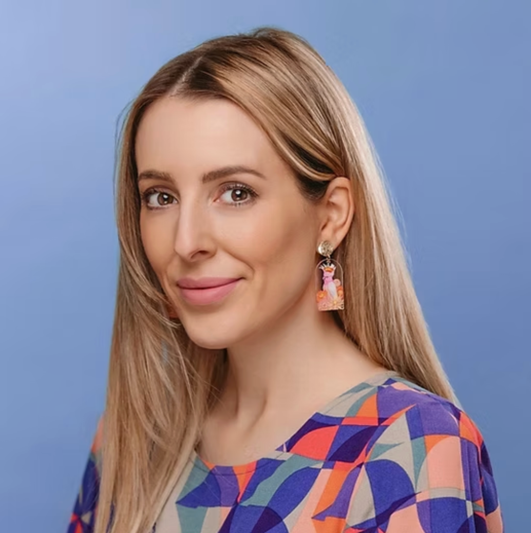 Portrait of a smiling woman with long blonde hair wearing a colorful patterned top against a blue background