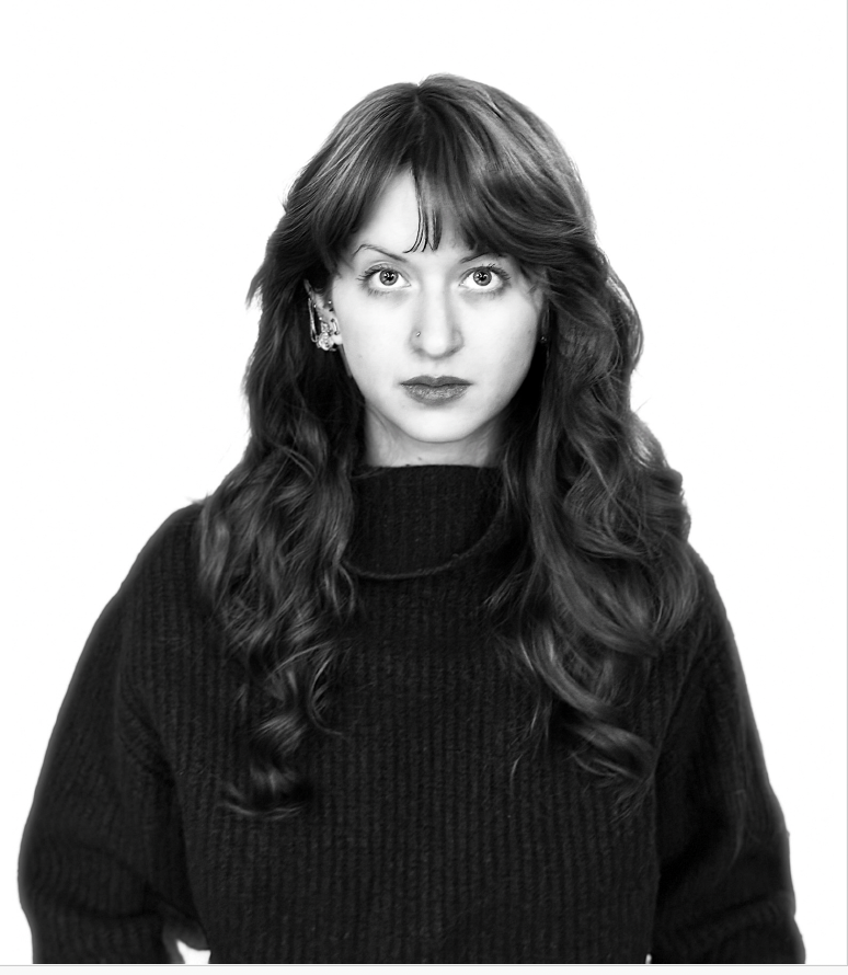 Black-and-white portrait of a person with wavy hair wearing a dark sweater, facing forward with a neutral expression