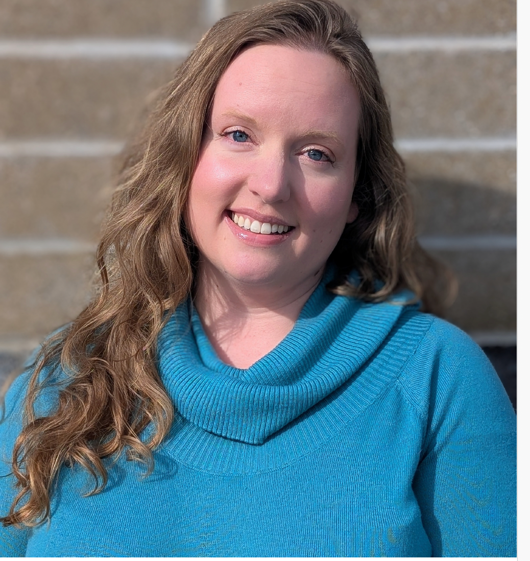Smiling woman in a bright blue sweater standing outdoors in front of a stone wall