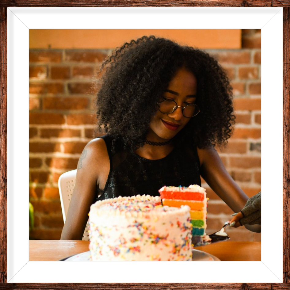 A woman is cutting a rainbow cake with sprinkles