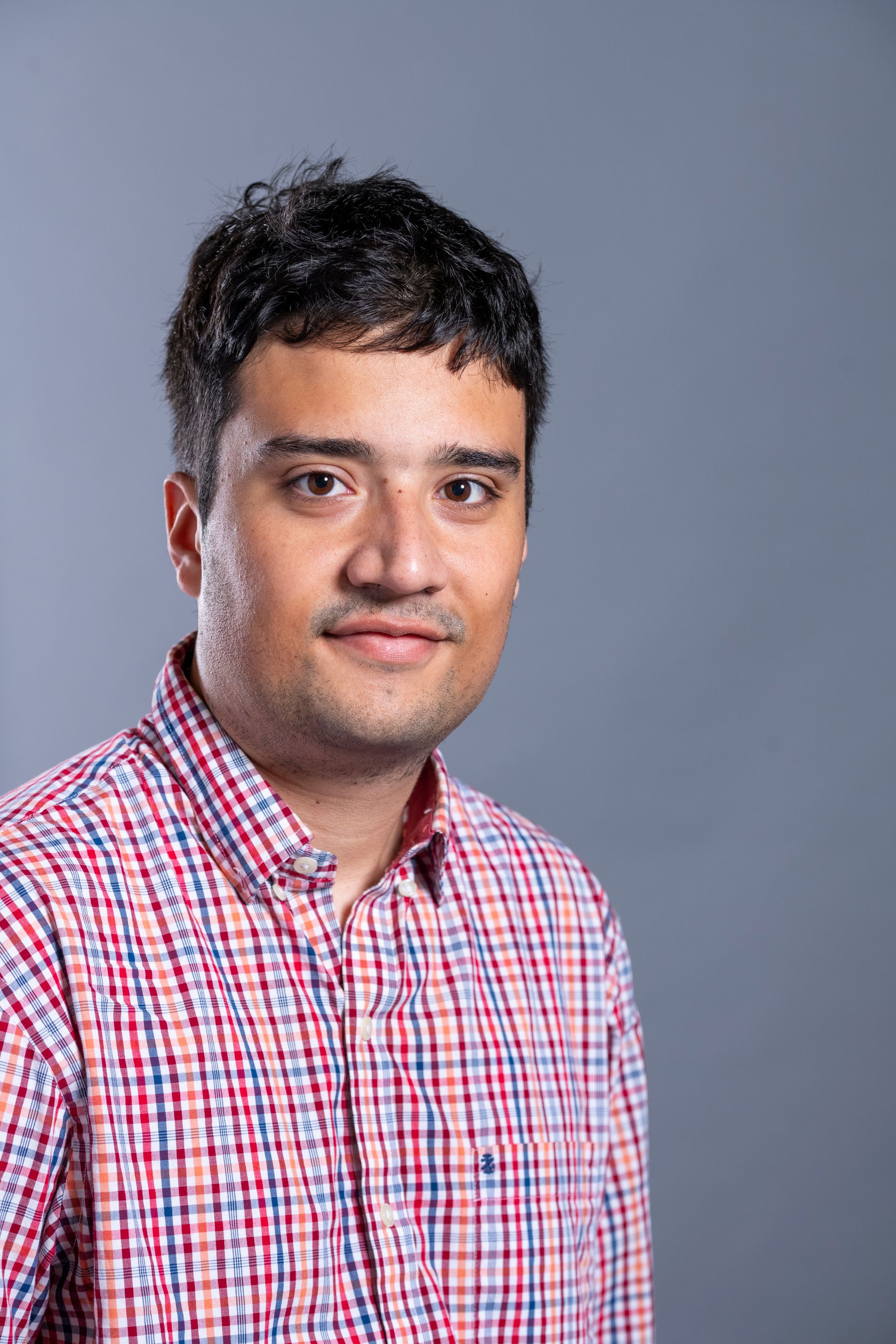 Man in a red plaid shirt posing against a gray studio backdrop