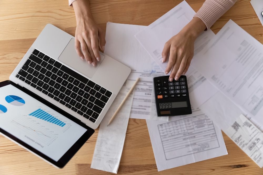 A woman is sitting at a table using a laptop and a calculator.