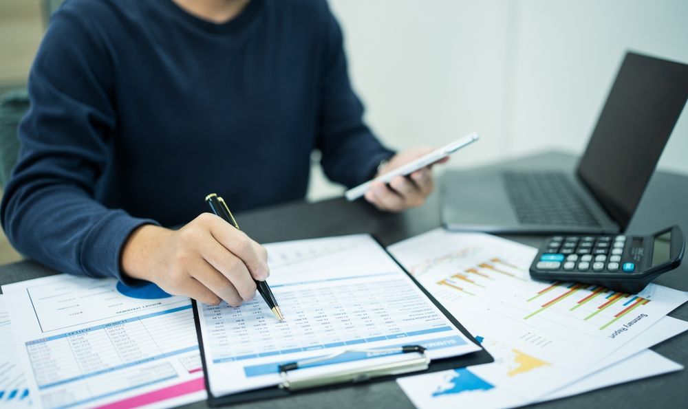 A man is sitting at a table using a tablet and a calculator.