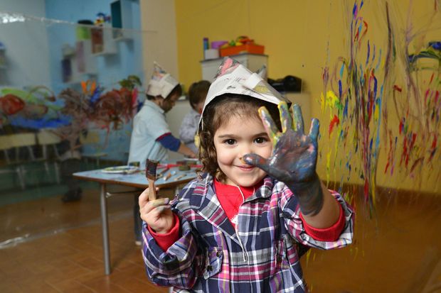Niño sonriendo con las manos cubiertas de pintura en una colorida actividad artística en el aula.