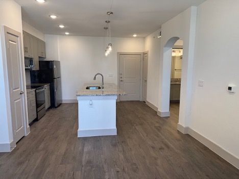 Empty modern kitchen with white cabinets, island, stainless appliances, and wood-look flooring