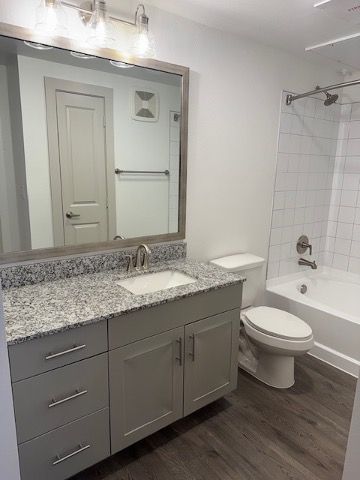 Modern bathroom with gray vanity, large mirror, white toilet, and tiled shower on dark wood floor