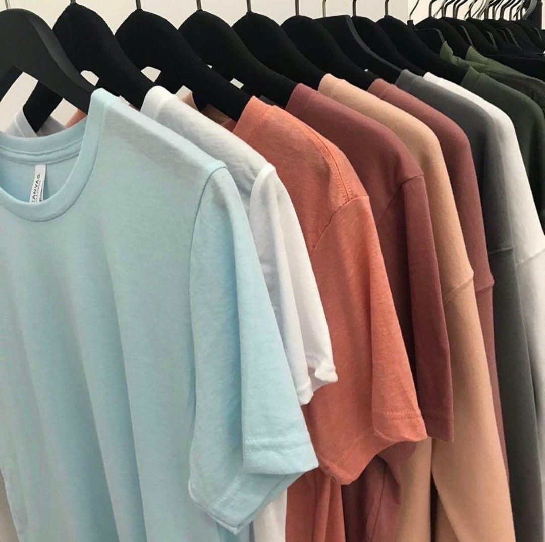 A row of t-shirts in different colors are hanging on a rack