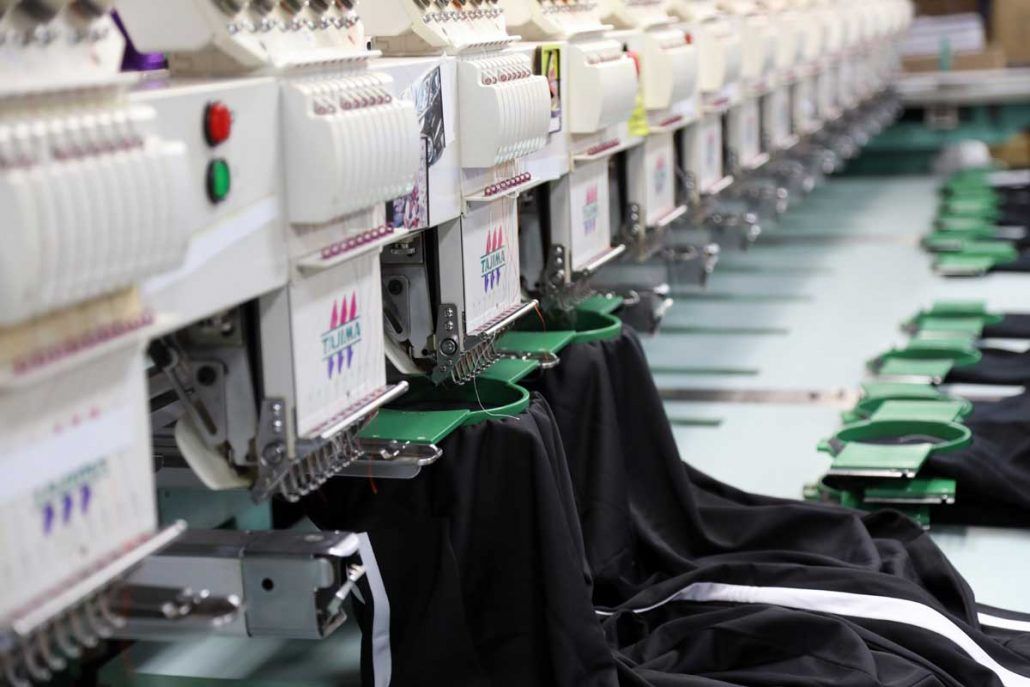 A row of embroidery machines are sitting next to each other in a factory.
