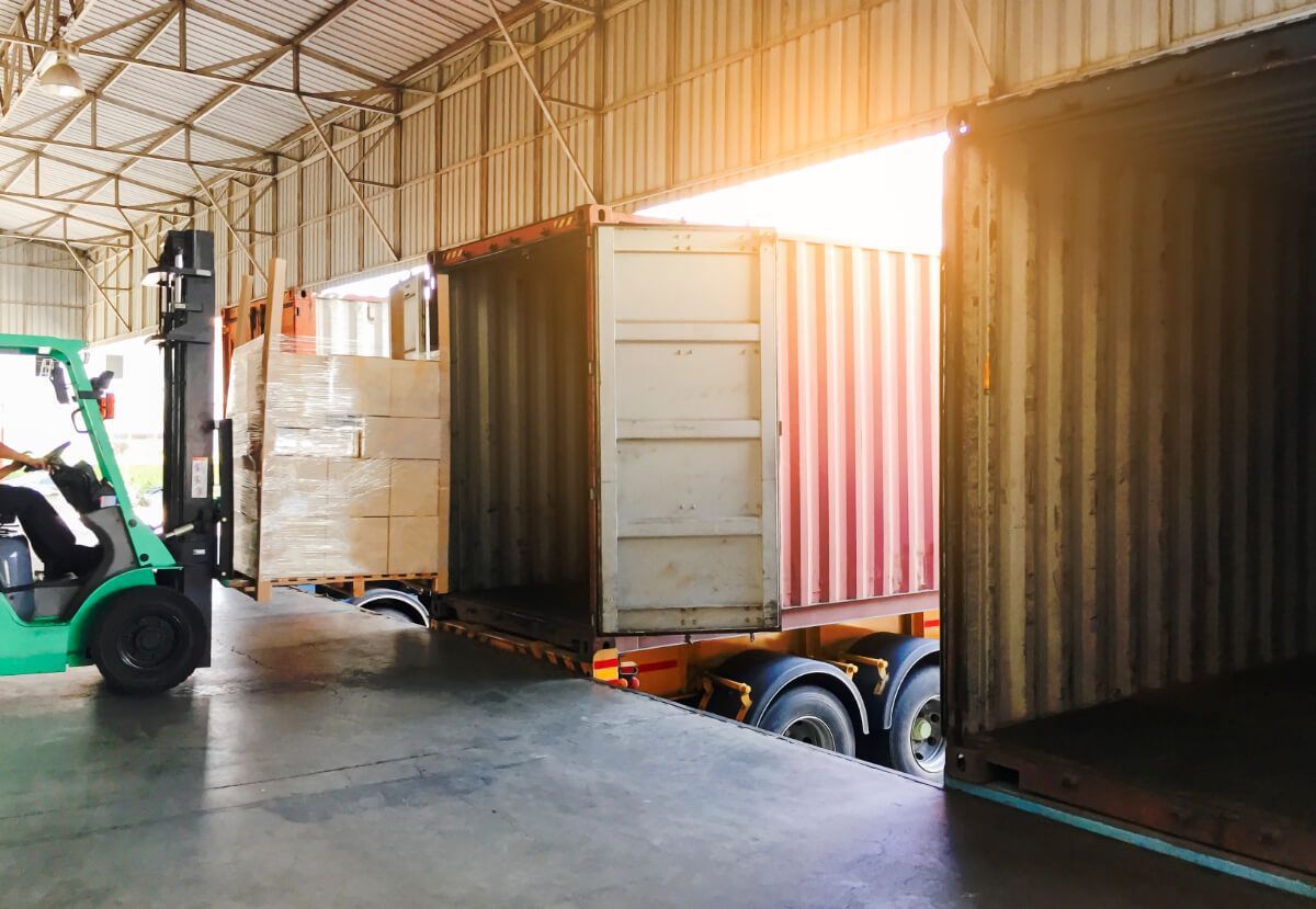 A forklift is loading a container into a truck in a warehouse.
