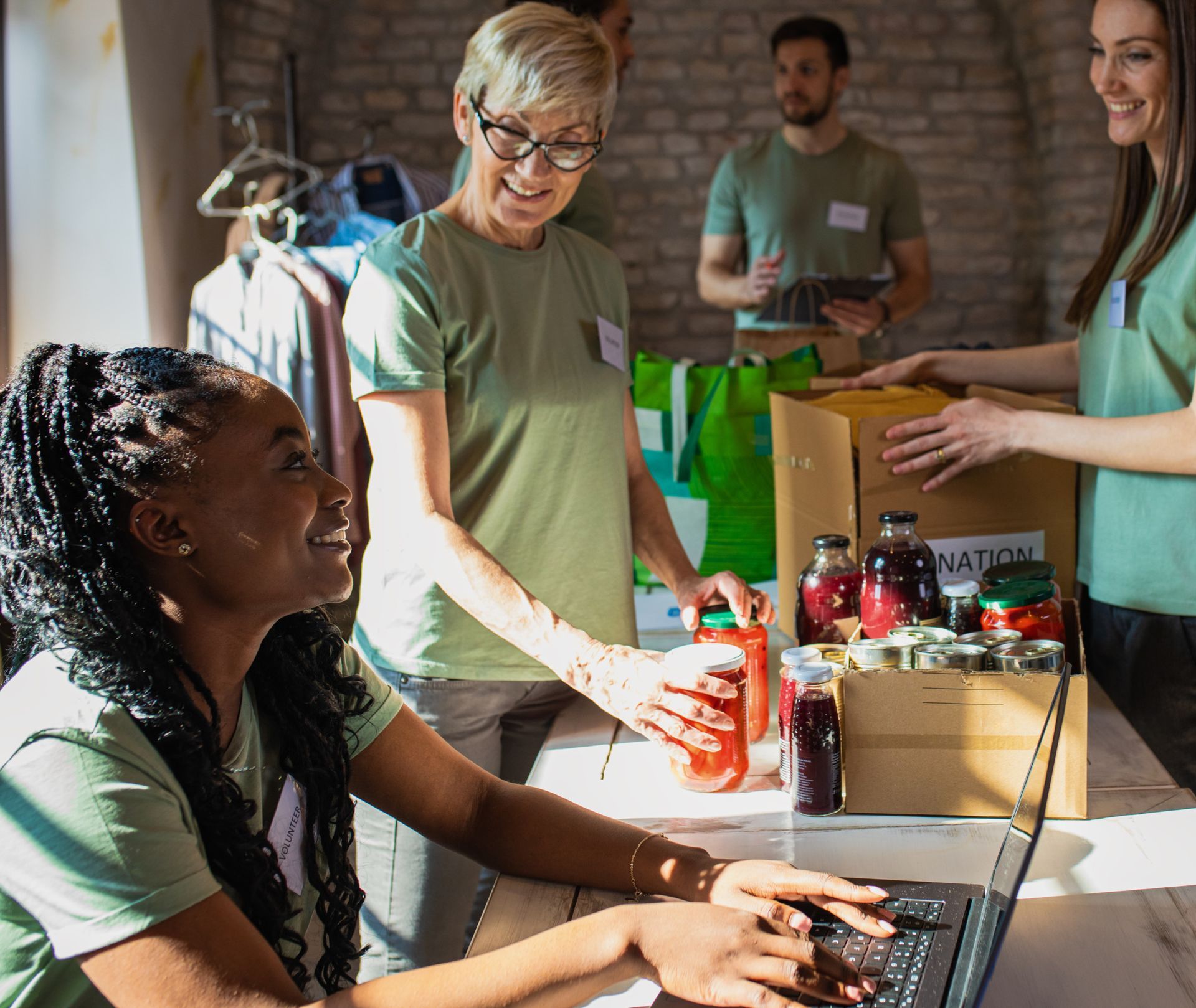 A woman is using a laptop computer while a group of people are standing around a table.