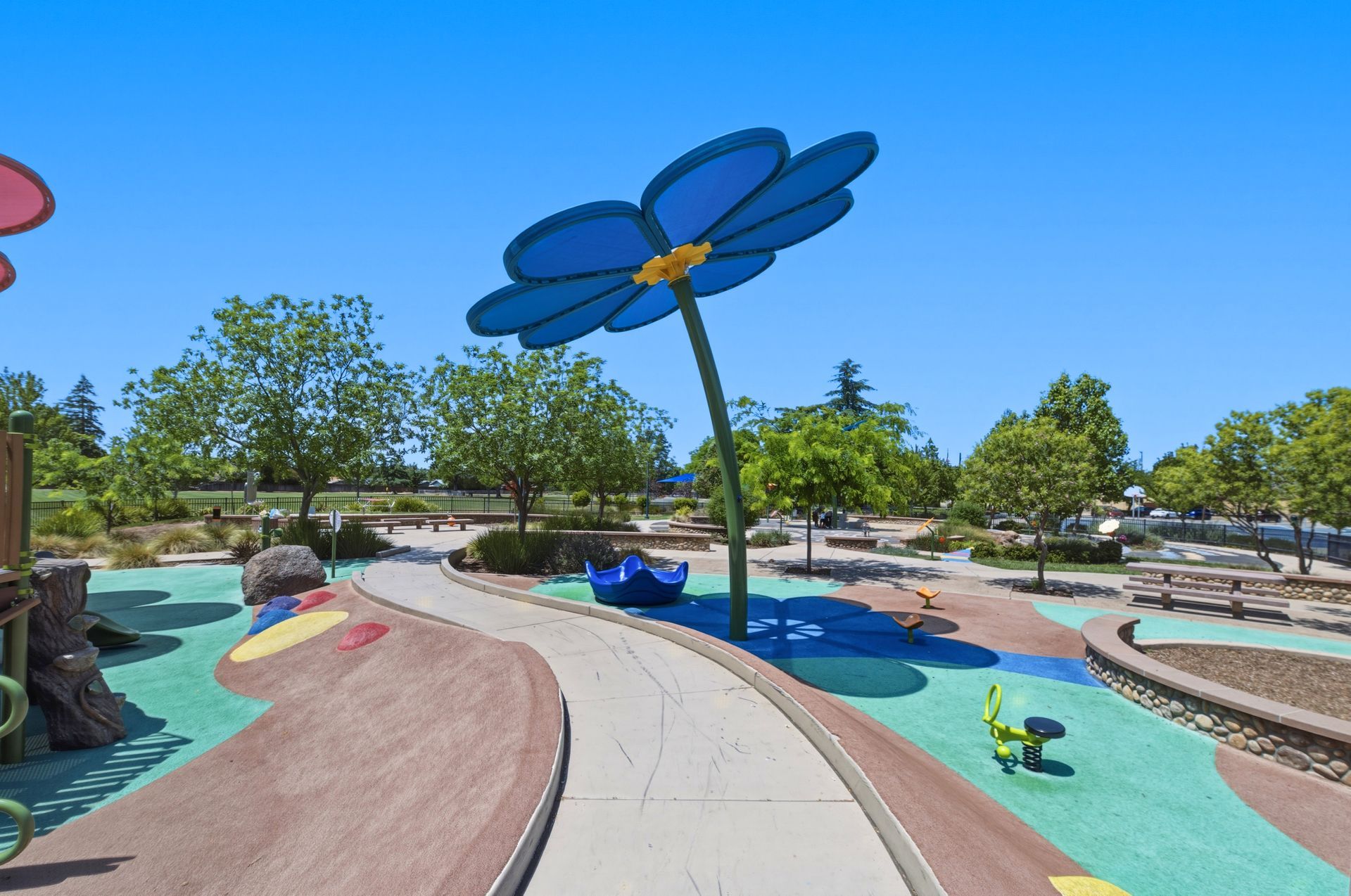 Colorful outdoor splash pad with oversized blue flower sprinklers under a clear sky
