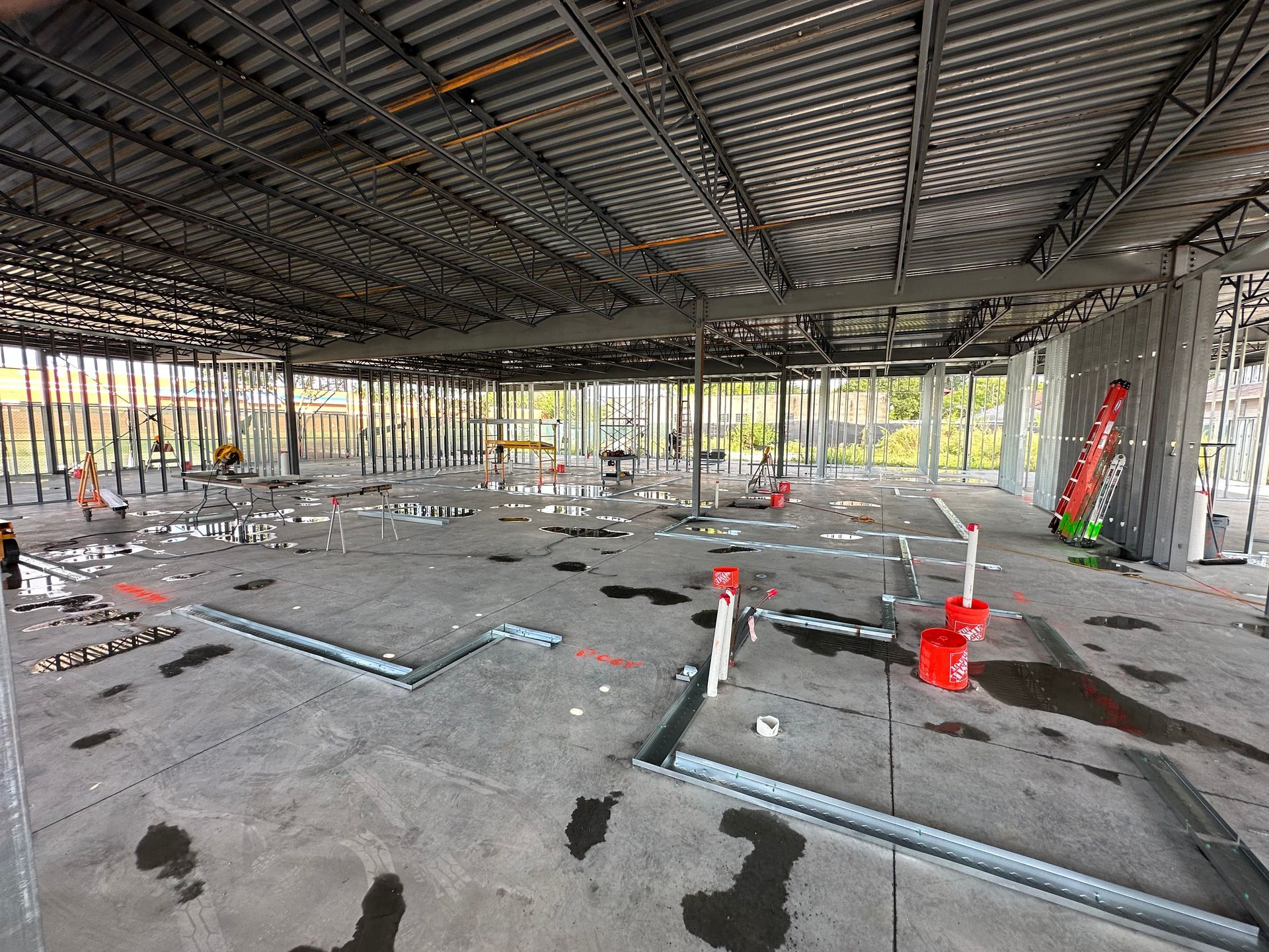 Interior of a construction site. Metal beams, concrete floor, visible pipes, and work in progress.