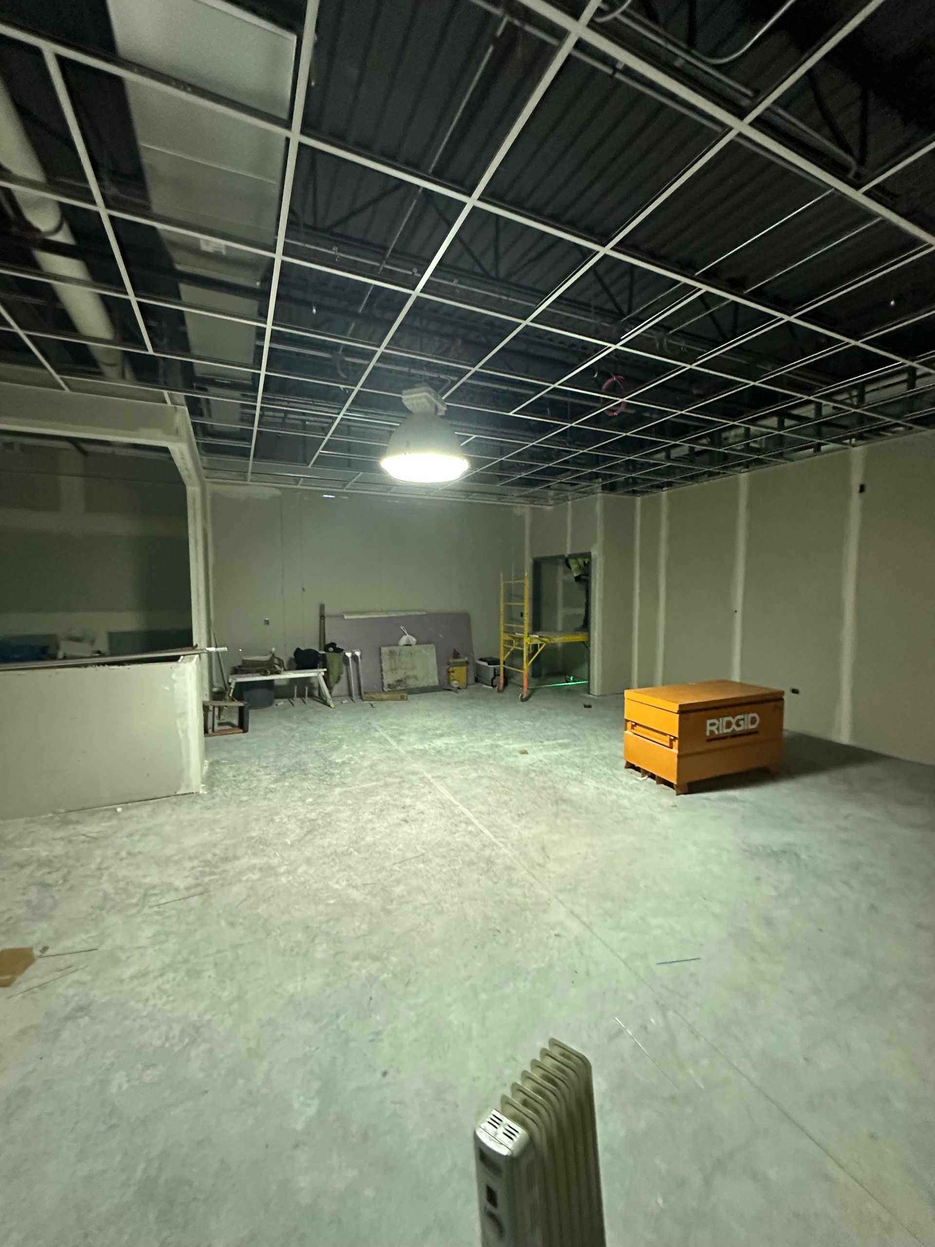 Interior of a construction site with exposed ceiling, unfinished walls, concrete floor, and an orange toolbox.