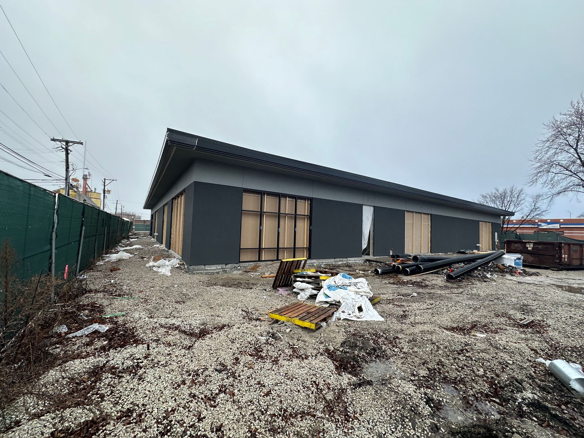 Building under construction; dark gray exterior, black roof, wooden door frames. Cloudy, outdoor setting.