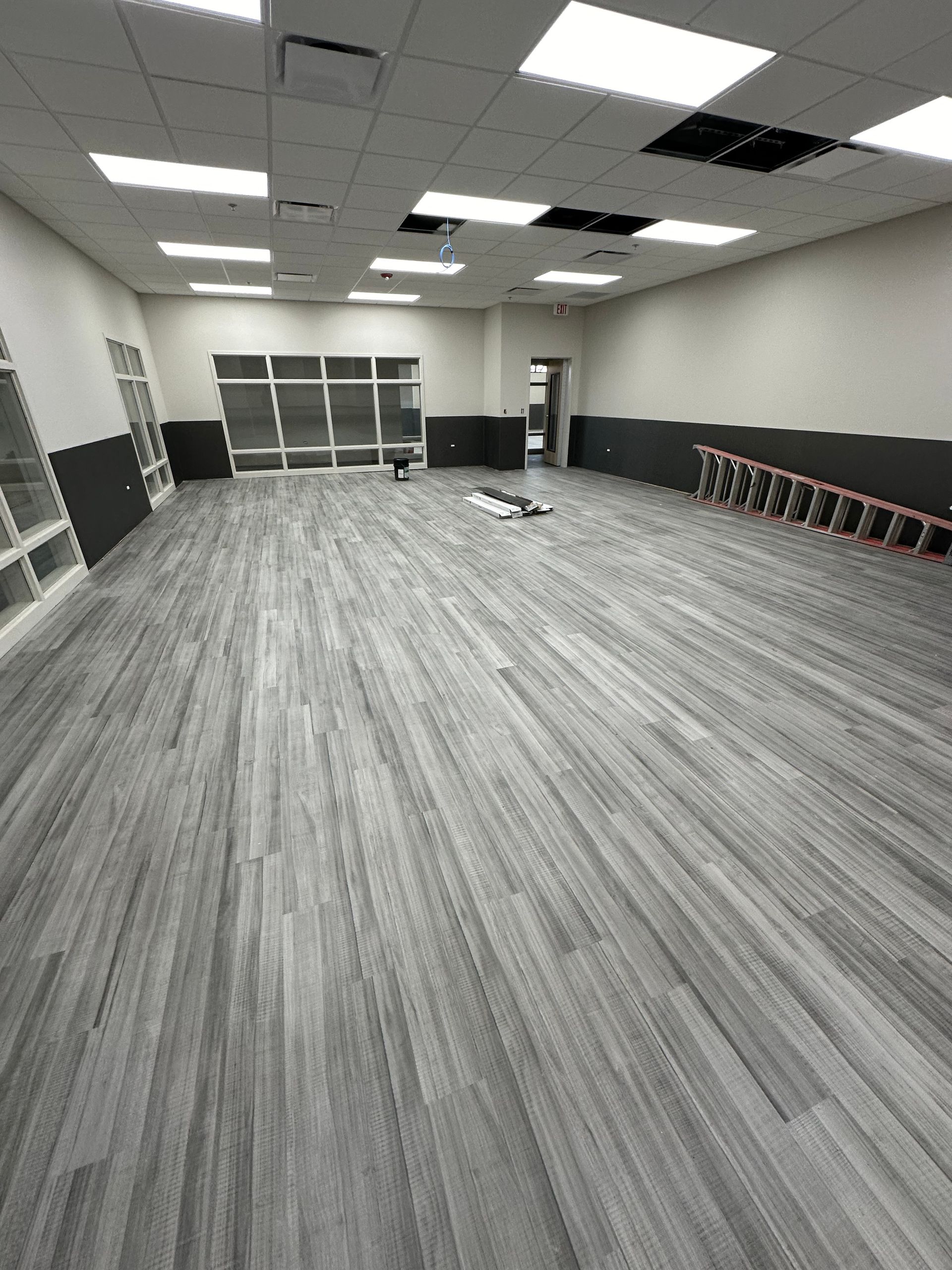 Empty room with gray wood-look flooring, white ceiling, and dark gray wall accents.
