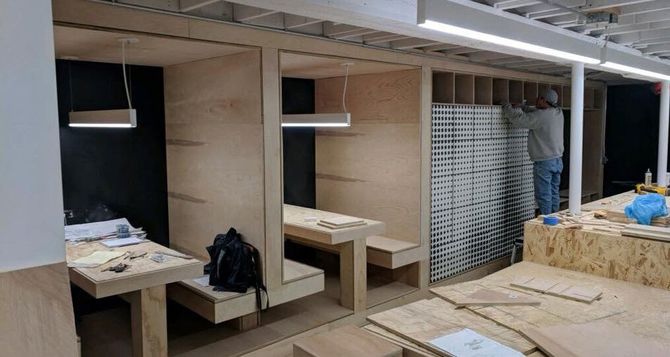 Construction of small wooden booths in an open space, with a worker installing a structure.