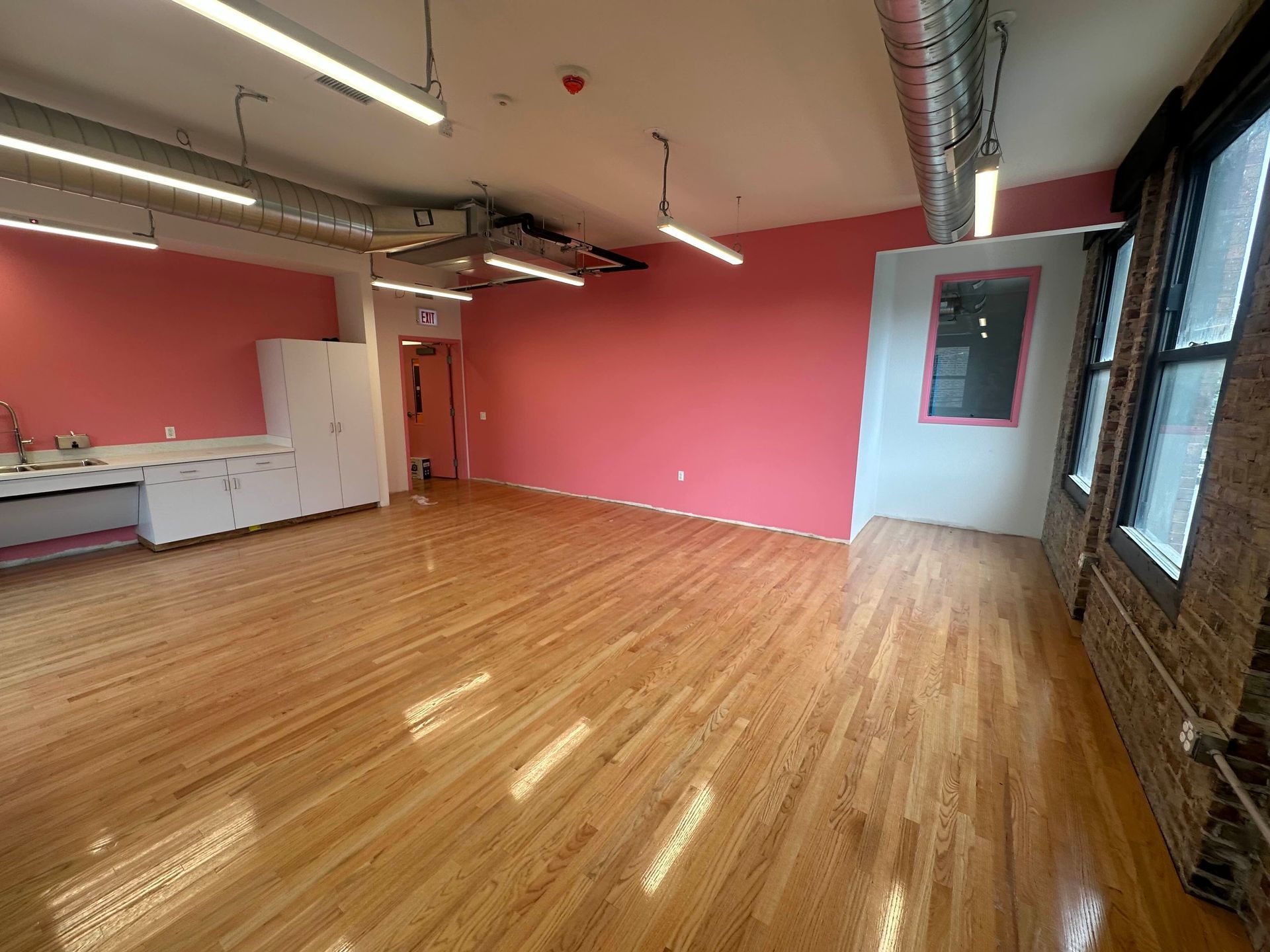 Empty room with pink walls, wood floors, and industrial-style exposed ceiling.