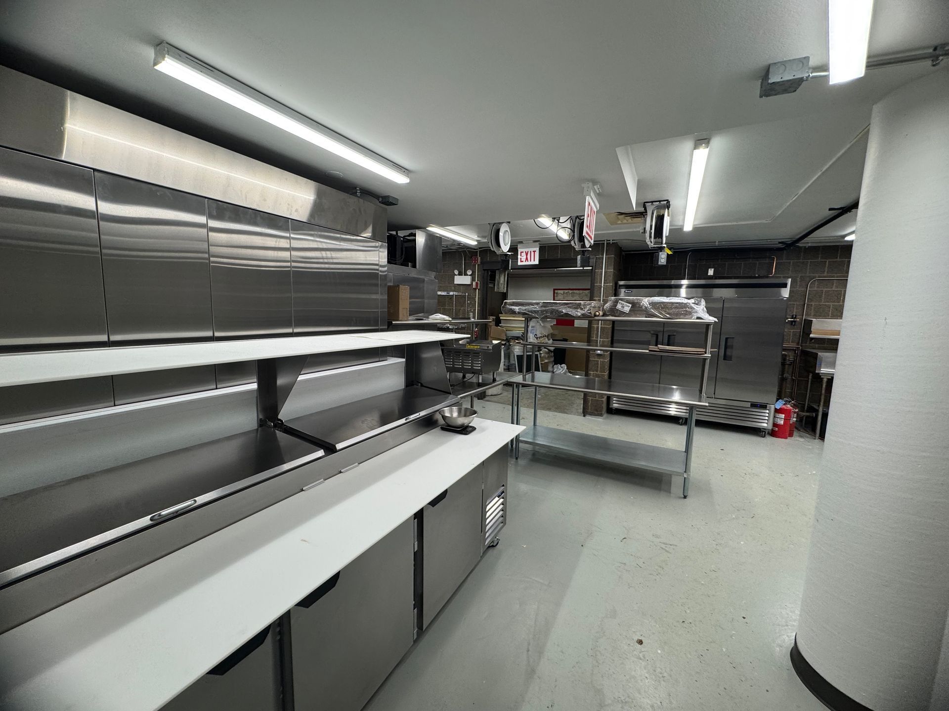Commercial kitchen interior with stainless steel equipment and shelves; white and gray.