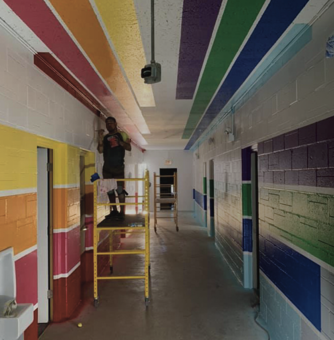 Man painting a hallway with rainbow stripes using a scaffold.