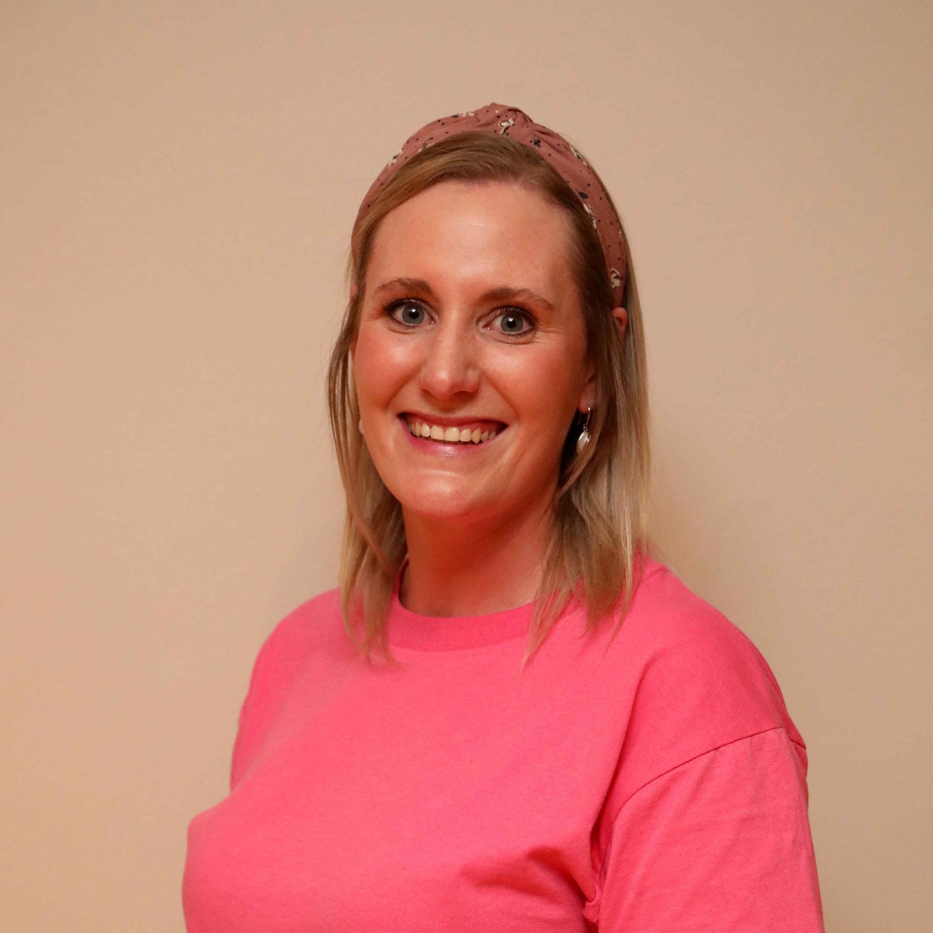 Smiling person in a bright pink shirt and matching headband against a plain beige wall