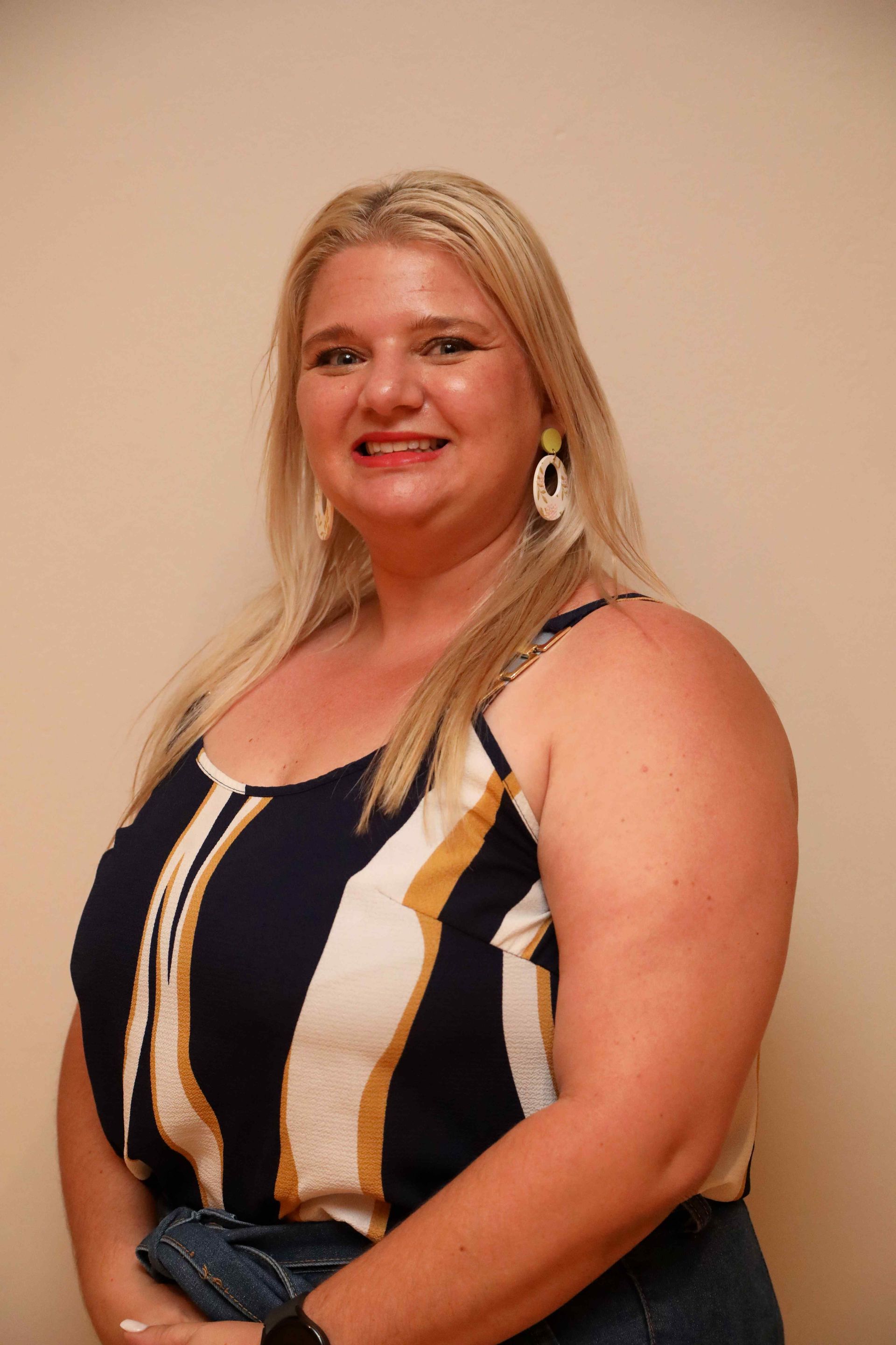 Smiling woman in a black, white, and tan striped sleeveless top against a plain beige wall