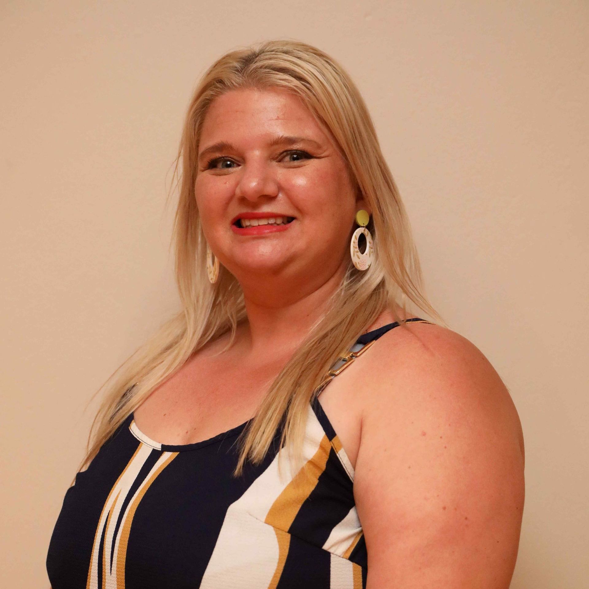 Smiling woman in a navy and white striped dress against a beige wall