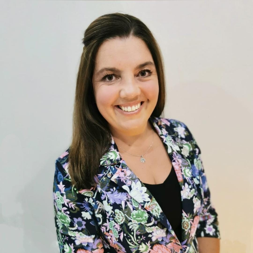 Smiling woman in a floral blazer standing against a light gray background