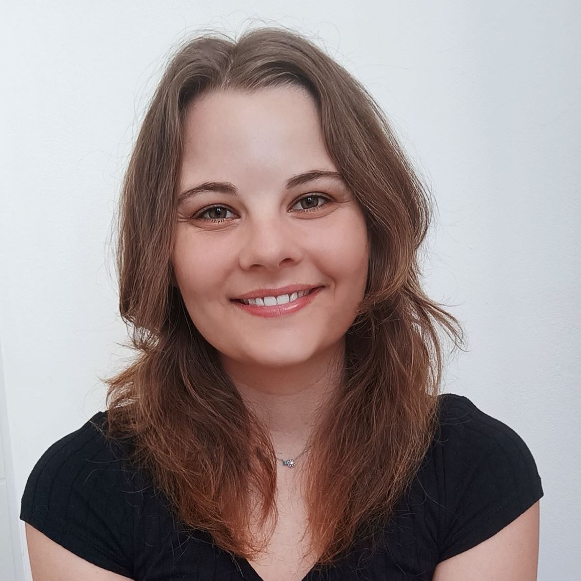 Smiling woman with shoulder-length brown hair wearing a black top against a light background